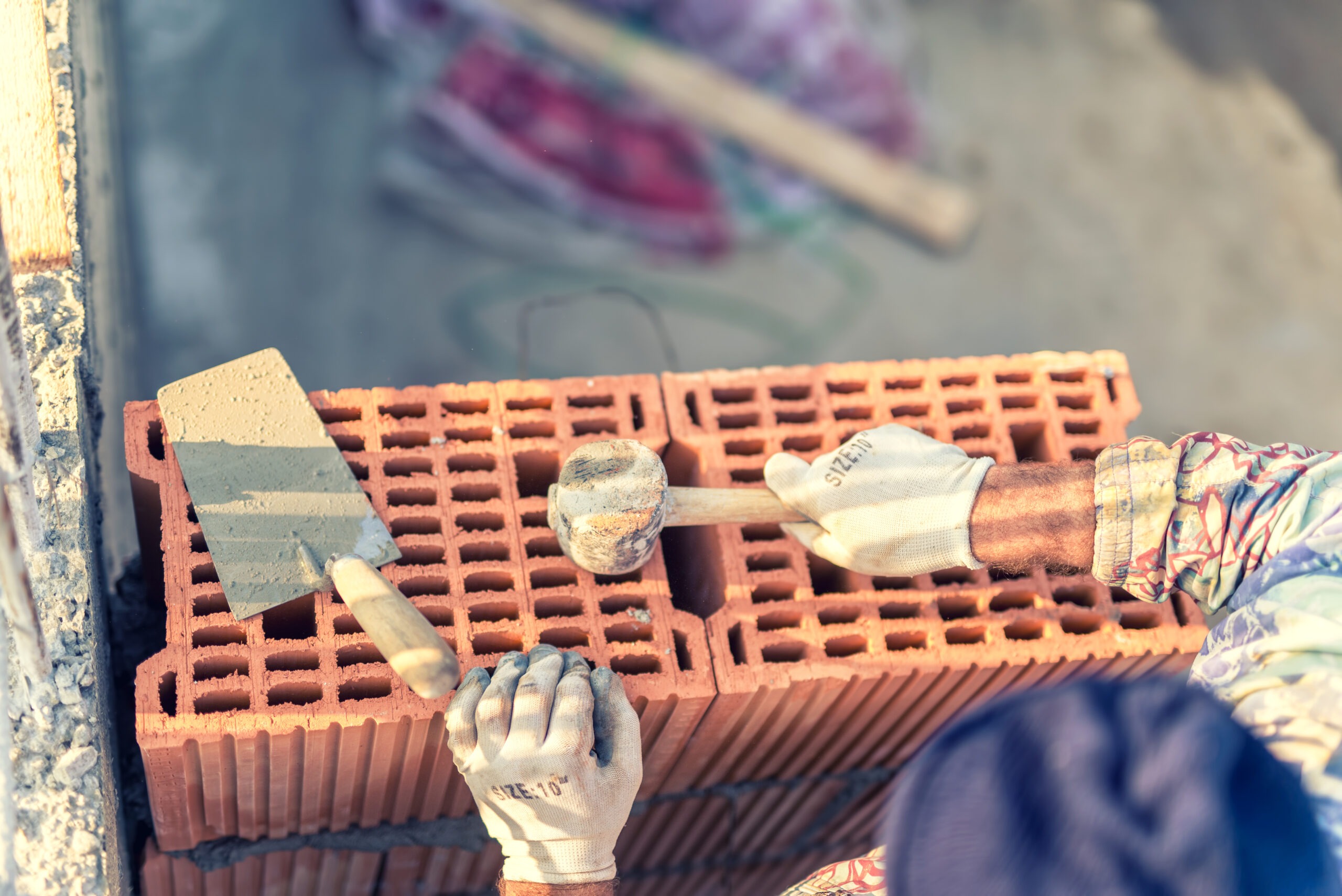 Construction worker building walls and fixing bricks with mortar and rubber hammer